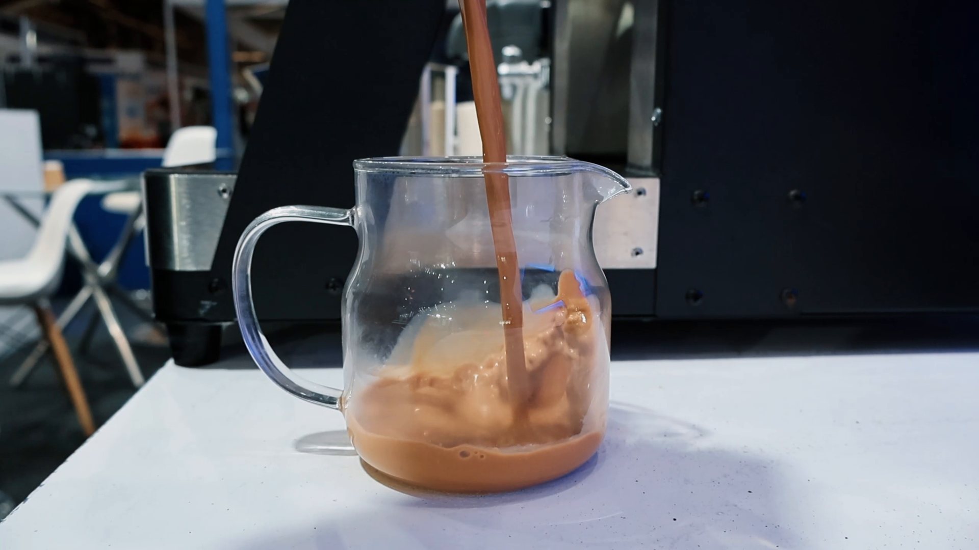 Freshly brewed chai being poured by hand from the pot into a glass serving jug